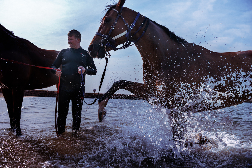 A trainer in a wetsuit holds the reins of two horses.